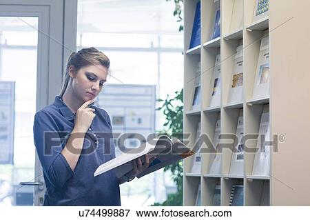 Young female student with hand on chin reading textbook in library View Large Photo Image Stock Photo - Young female student with hand on chin reading textbook in library. Fotosearch