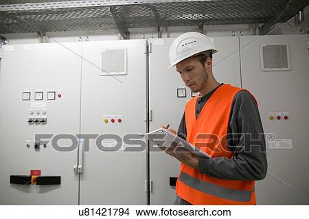 Young male engineer reading paperwork in technical room View Large Photo Image Picture - Young male engineer reading paperwork in technical room. Fotosearch