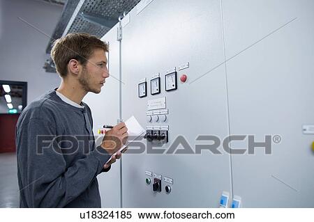 Stock Photography - Young male technician making notes in technical room. Fotosearch