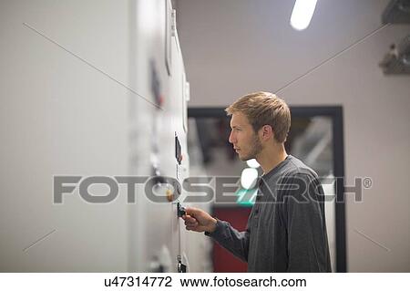 Stock Image - Young male technician turning switch in technical room. Fotosearch