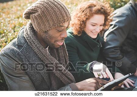 Young man and woman using touchscreen on digital tablet in park View Large Photo Image Stock Image - Young man and woman using touchscreen on digital tablet in park. Fotosearch