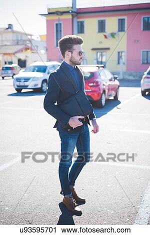 Stock Image - Young man carrying briefcase walking across parking lot. Fotosearch