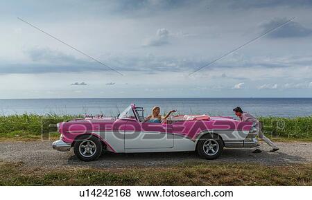 Stock Photo - Young man pushing vintage convertible at coast whilst girlfriend drives, Havana, Cuba. Fotosearch