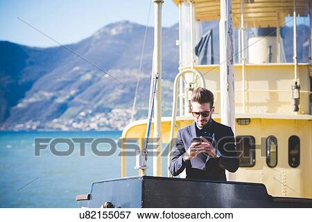 Stock Photo - Young man reading smartphone texts from lake ferry, Rovato, Brescia, Italy. Fotosearch