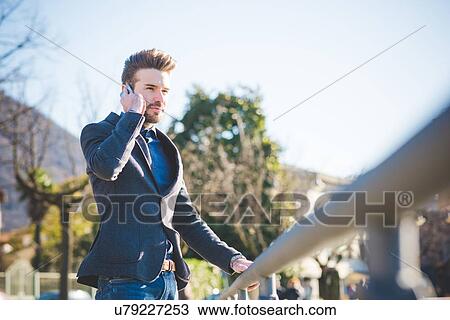 Stock Image - Young man talking on smartphone whilst holding railing. Fotosearch