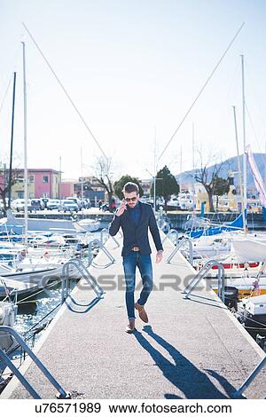 Young man talking on smartphone whilst walking on lake pier View Large Photo Image Stock Photo - Young man talking on smartphone whilst walking on lake pier. Fotosearch
