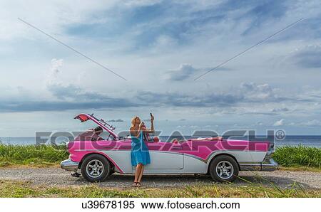 Young man trying to fix a vintage convertible at coast whilst girlfriend putting on make up, Havana, Cuba View Large Photo Image Stock Photography - Young man trying to fix a vintage convertible at coast whilst girlfriend putting on make up, Havana, Cuba. Fotosearch