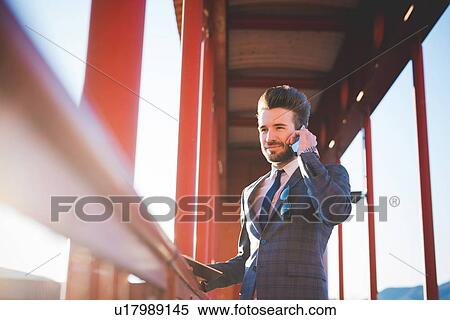 Young man with digital tablet chatting on smartphone on footbridge View Large Photo Image Stock Photography - Young man with digital tablet chatting on smartphone on footbridge. Fotosearch
