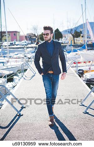 Stock Photo - Young man with hand in pocket walking on lake pier. Fotosearch