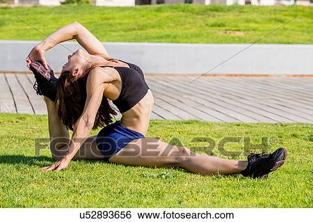 Stock Photograph - Young woman doing stretches in park. Fotosearch