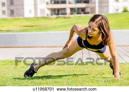 Stock Image - Young woman exercising in park. Fotosearch
