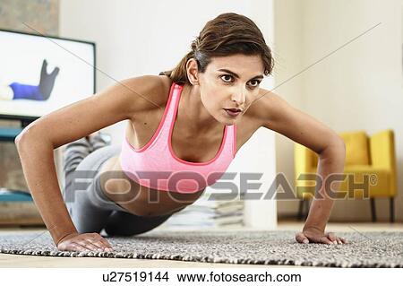 Picture - Young woman exercising on living room floor in front of computer screen. Fotosearch