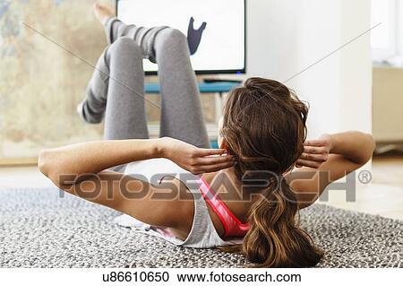 Stock Image - Young woman exercising on living room floor following computer screen instruction. Fotosearch