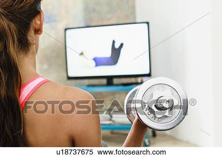 Young woman exercising with hand weights in living room whilst watching computer screen View Large Photo Image Stock Photography - Young woman exercising with hand weights in living room whilst watching computer screen. Fotosearch