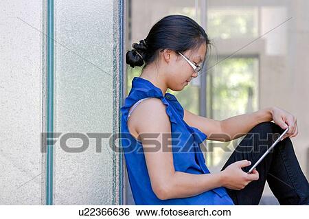 Young woman leaning against wall reading digital tablet View Large Photo Image Stock Photograph - Young woman leaning against wall reading digital tablet. Fotosearch