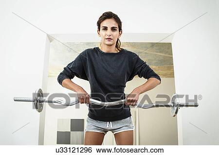 Young woman lifting barbell in living room View Large Photo Image Stock Photograph - Young woman lifting barbell in living room. Fotosearch