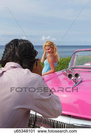 Stock Image - Young woman posing for photographs with vintage convertible, Havana, Cuba. Fotosearch