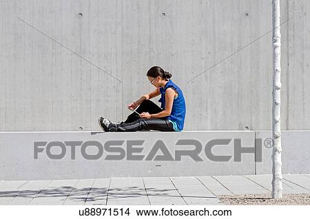 Picture - Young woman sitting on wall reading digital tablet. Fotosearch