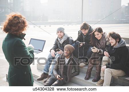 Stock Photo - Young woman using laptop in front of friends on steps. Fotosearch