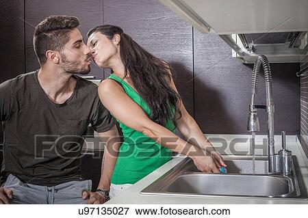 Stock Photo - Young woman washing up whilst kissing boyfriend. Fotosearch