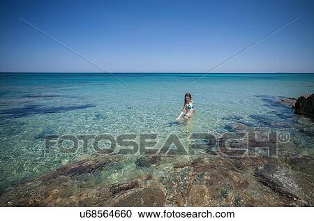 Stock Image - Young woman wearing bikini wading in sea, Cagliari, Sardinia, Italy. Fotosearch