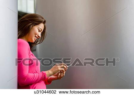 Young woman wearing pink tshirt leaning against pillar reading smartphone texts View Large Photo Image Stock Image - Young woman wearing pink tshirt leaning against pillar reading smartphone texts. Fotosearch