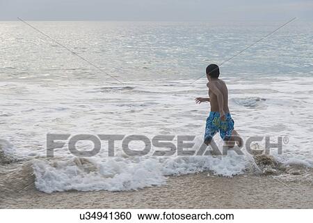 Stock Image - Boy running in waves on beach, Ixtapa, Guerrero, Mexico. Fotosearch