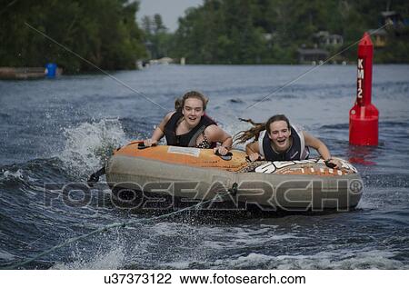 Stock Image - Portrait of two girls lying on an inflatable raft floating in a lake, Lake Of The Woods, Ontario, Canada. Fotosearch