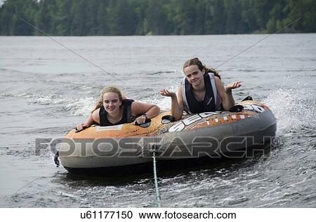 Stock Image - Portrait of two girls lying on an inflatable raft floating in a lake, Lake Of The Woods, Ontario, Canada. Fotosearch
