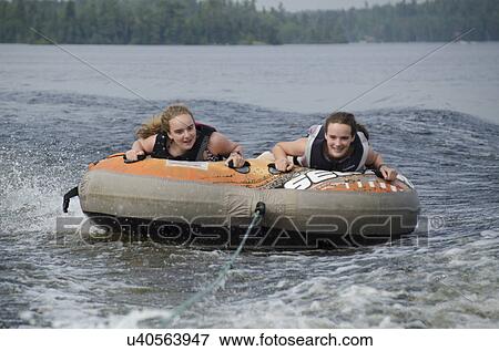 Stock Photo - Portrait of two girls lying on an inflatable raft floating in a lake, Lake Of The Woods, Ontario, Canada. Fotosearch