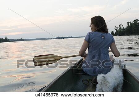 Stock Photograph - Rear view of a woman rowing boat with puppy in lake, Lake of the Woods, Ontario, Canada. Fotosearch