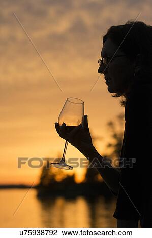Stock Image - Silhouette of woman holding a wineglass, Lake of the Woods, Ontario, Canada. Fotosearch
