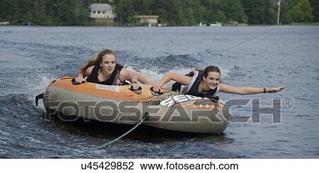 Stock Image - Two girls lying on an inflatable raft floating in a lake, Lake Of The Woods, Ontario, Canada. Fotosearch