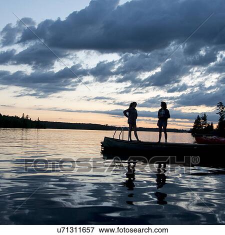 Two Woman standing on dock at dusk, Lake of the Woods, Ontario, Canada View Large Photo Image Stock Photo - Two Woman standing on dock at dusk, Lake of the Woods, Ontario, Canada. Fotosearch