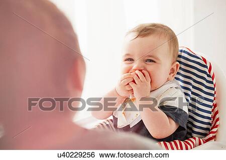 Baby boy feeding himself in baby chair View Large Photo Image Stock Photograph - Baby boy feeding himself in baby chair. Fotosearch