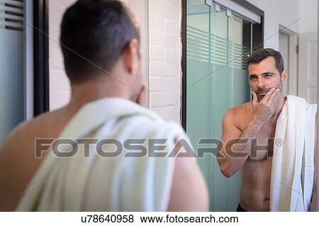 Stock Photo - "Bare chested mature man looking in mirror, hand on chin, touching stubble, towel over shoulder". Fotosearch