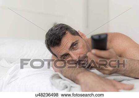 Bare shouldered mature man lying on front on bed using remote control View Large Photo Image Stock Photo - Bare shouldered mature man lying on front on bed using remote control. Fotosearch