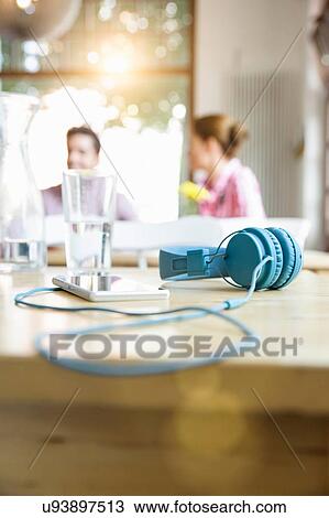 Stock Image - "Blue headphones attached to smartphone on table, people in the background". Fotosearch