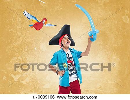 Stock Photograph - "Boy wearing pirate costume and eye patch holding balloon sword and lollipop, looking at camera smiling". Fotosearch