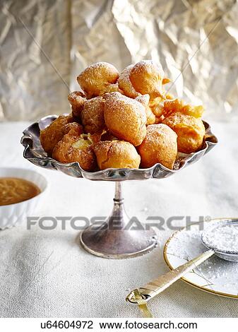 Stock Image - Bunuelos piled into silver serving dish dusted with icing sugar. Fotosearch