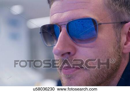 Stock Image - Close up of computer screen reflection in engineers sunglasses at geothermal power station. Fotosearch