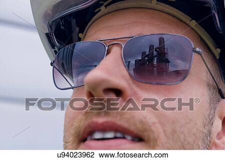 Stock Image - Close up of industrial structures reflected in engineers sunglasses at geothermal power station. Fotosearch