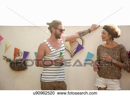 Couple holding drinks standing talking in front of wall decorated with bunting View Large Photo Image Stock Image - Couple holding drinks standing talking in front of wall decorated with bunting. Fotosearch