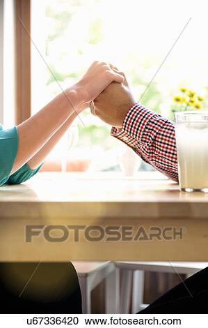 Stock Image - Cropped shot side view of couple holding hands across table. Fotosearch