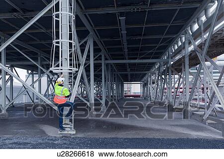 Stock Photo - Engineer climbing ladder in warehouse space at geothermal power station. Fotosearch