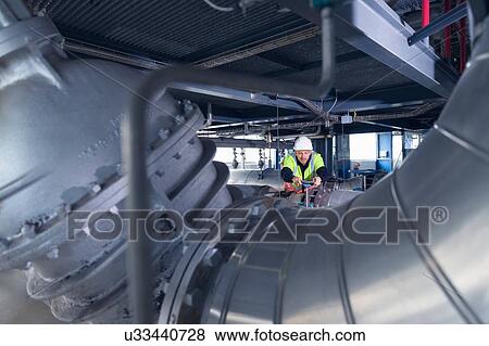 Stock Photo - Engineer inspecting pipes at geothermal power station. Fotosearch