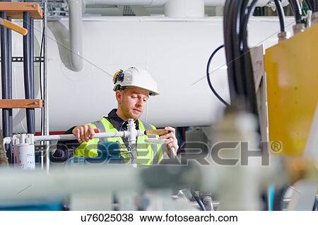 Stock Photo - Engineer maintaining industrial equipment at geothermal power station. Fotosearch