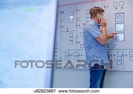 Engineer pointing at control panel whilst talking on smartphone at geothermal power station View Large Photo Image Stock Photo - Engineer pointing at control panel whilst talking on smartphone at geothermal power station. Fotosearch