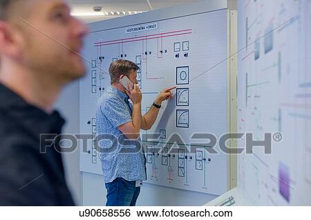 Stock Photograph - Engineer pointing at control panel whilst using smartphone at geothermal power station. Fotosearch