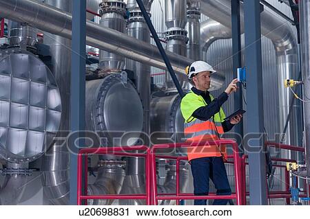 Stock Image - Engineer using digital tablet whilst using switch in geothermal power station. Fotosearch